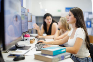 Mehrere Studierende sitzen in einer Fachbibliothek und lernen mit Büchern und Bildschirmen