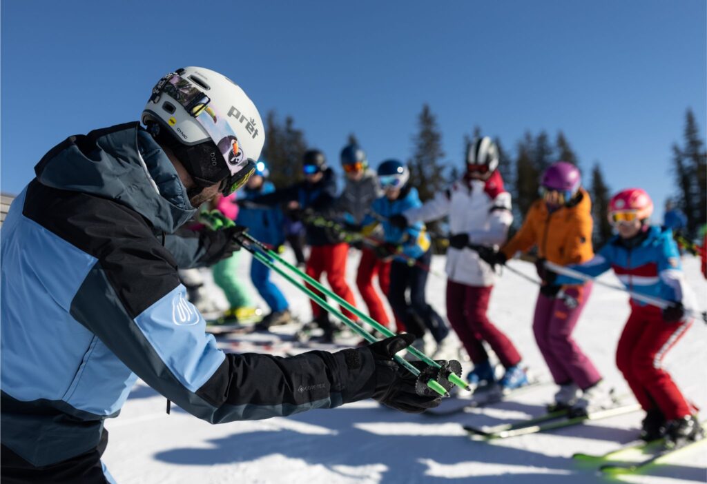 Ein*e Skilehrer*in zeigt vor der Gruppe eine Übung vor.